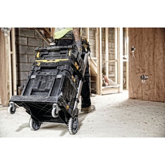DEWALT stackable tool boxes on a wheeled trolley in a construction area being moved by a worker.