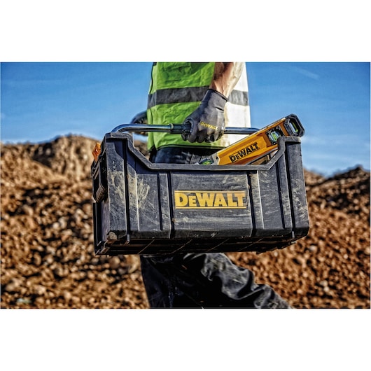 Worker carrying a DEWALT toolbox with tools outdoors at a construction site.