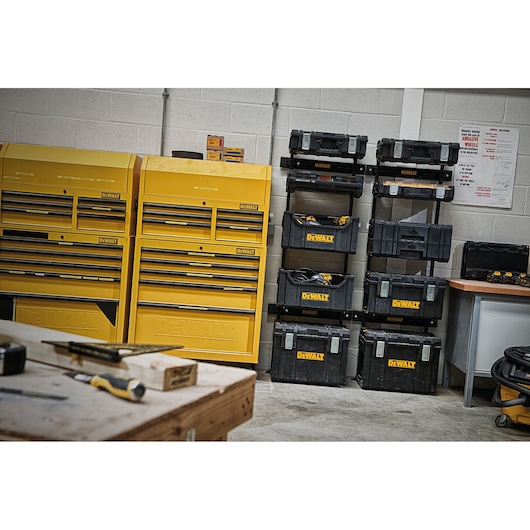 DEWALT storage boxes and tool cabinets stacked in a workshop with tools on a bench in the foreground.