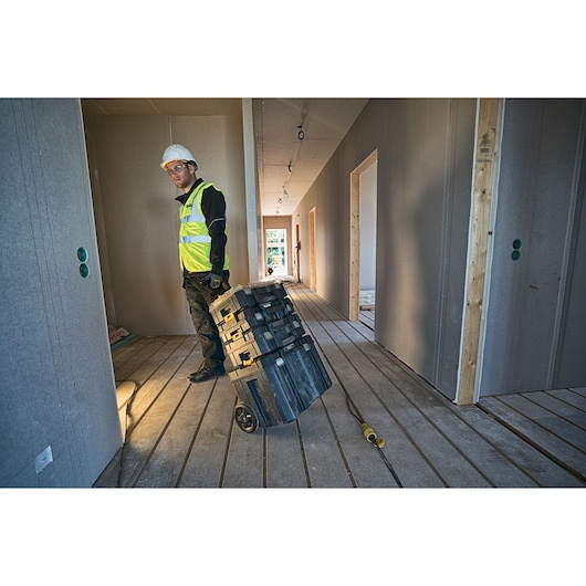 Worker with DEWALT stackable toolboxes on wheels inside a building under construction.