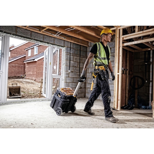Worker pulls DEWALT DWST1-75799 tool box on wheels inside building under construction.