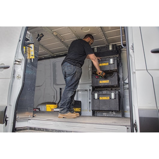 A person organizes DEWALT storage boxes inside a van used for transporting tools and equipment.