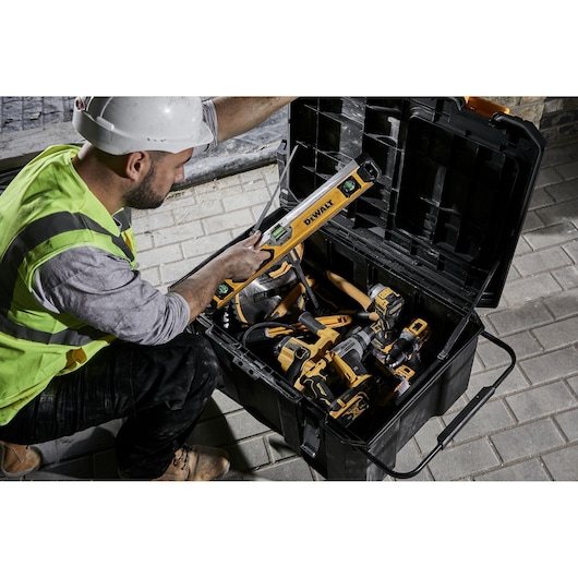 Person with safety gear uses DEWALT tool from a large toolbox full of yellow and black DEWALT power tools.
