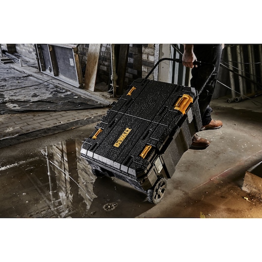 DEWALT wheeled toolbox being pulled by a person in a wet, industrial workspace.