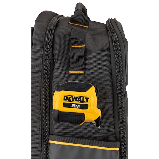 Close-up of a black and yellow DEWALT tape measure attached to a black tool bag with zippered compartments.