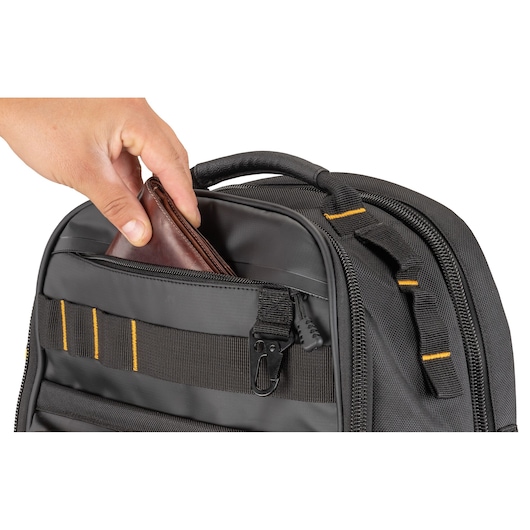 A hand is placing a brown wallet into the front zippered pocket of a black DEWALT photography backpack with yellow accents.