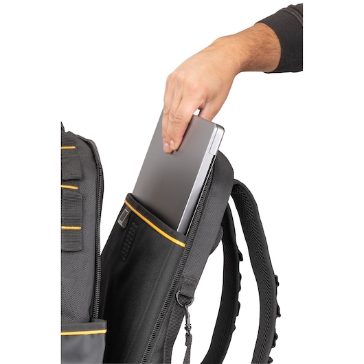A person is placing a laptop into the padded compartment of a black DEWALT backpack with yellow accents.