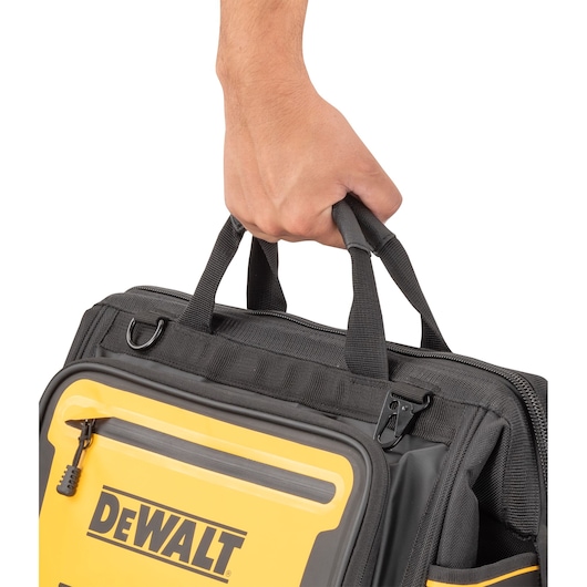 A close-up of a person’s hand holding the handles of a DEWALT-branded black and yellow tool bag.