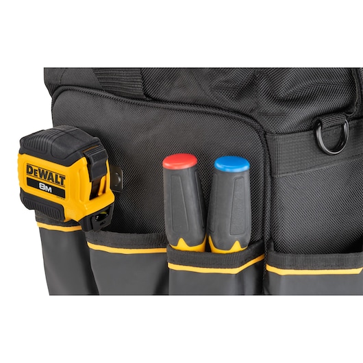 Close-up of a black DEWALT tool bag showing a yellow DEWALT 8m tape measure and two hand tools with black handles, one with a red cap and one with a blue cap, in the front pockets.