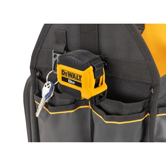 Close-up of a DEWALT tape measure and a set of keys placed in the pocket of a black and yellow tool bag.