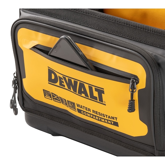 Close-up of a DEWALT bag's yellow and black water-resistant front compartment with a phone partially placed inside the zippered pocket.