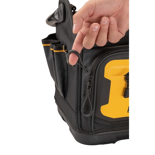 A close-up of a hand holding a zipper pull on a black and yellow DEWALT tool bag with external tool pockets.