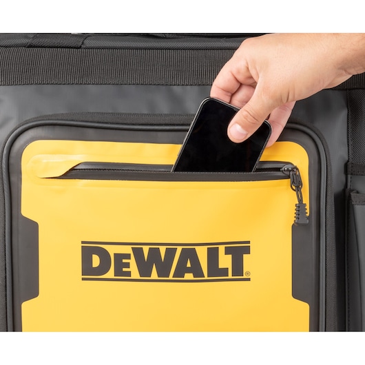 A hand placing a smartphone into the front zippered pocket of a yellow and black DEWALT branded bag.