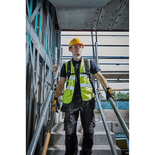 Person in safety gear and gloves walking on stairs at construction site with metal scaffold.