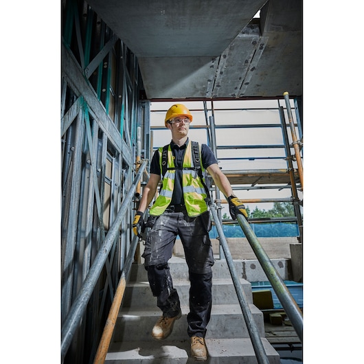 Worker in safety gear on stairs at construction site with DEWALT vest and helmet.