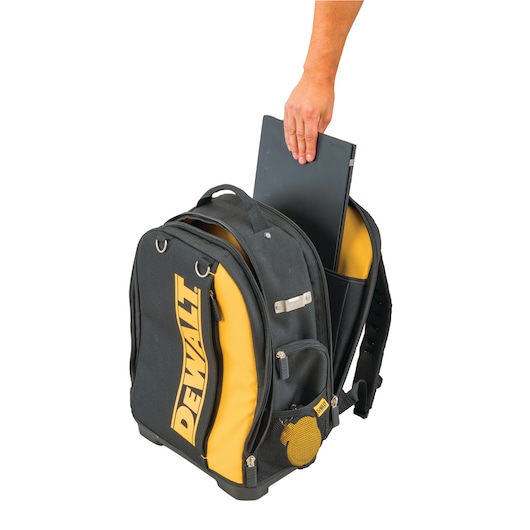 Hand placing a laptop into a black and yellow DEWALT backpack with multiple compartments.