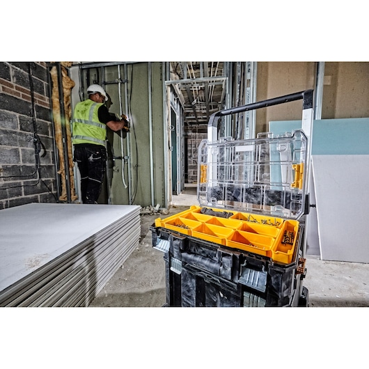 Dewalt organizer box with yellow compartments open on a construction site, worker in background.