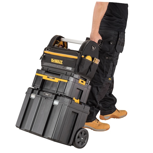 Person pulls a stacked DEWALT rolling toolbox set with tool bag, wearing work clothes and boots.