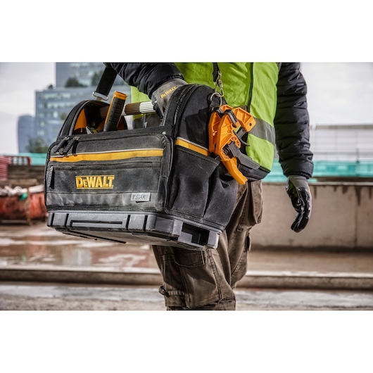 DEWALT tool bag with tools, carried by a worker in outdoor construction setting.