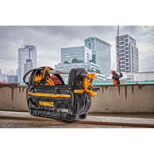 DEWALT tool bag with tools on a construction site, city buildings in background.