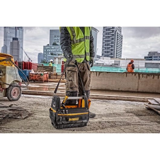 DEWALT tool bag with handle seen on a construction site, carried by a worker in a safety vest and gloves.