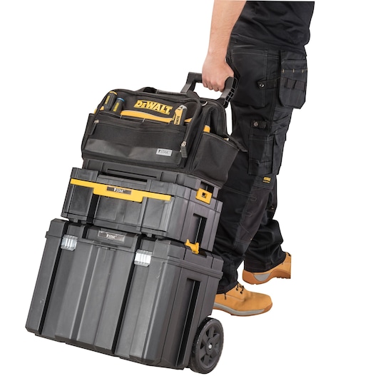 Person pulling DEWALT stackable toolboxes with wheels and handle. Tool bag is on top. All boxes are black and yellow.