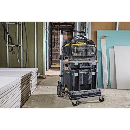 DEWALT tool trolley with stacked toolboxes and bag in a construction site with drywall sheets on the floor.