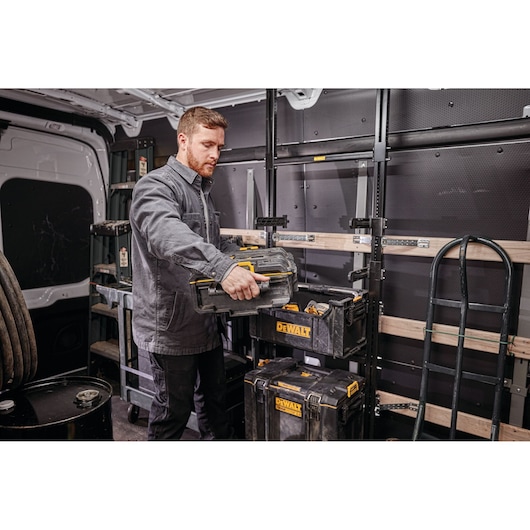 Person organizing DEWALT toolboxes in a van with racks and equipment.