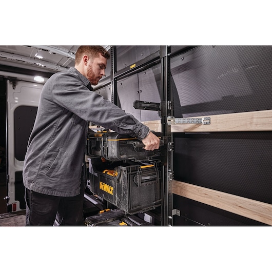 Person organizing DEWALT toolboxes on a shelving system inside a work van.