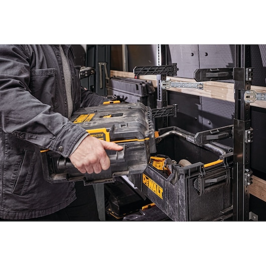 Person places a DEWALT toolbox onto modular rack system inside a workshop or utility vehicle.