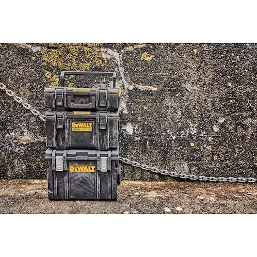 Stacked DEWALT ToughSystem 2.0 toolboxes against a rough wall with a metal chain in the background.