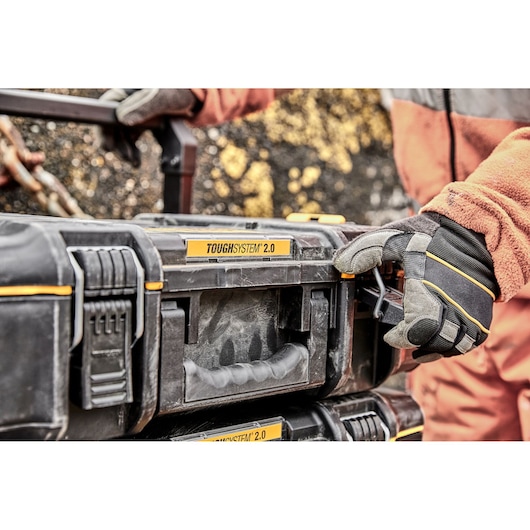Gloved hand operating a DEWALT ToughSystem 2.0 toolbox outdoors with rugged construction.