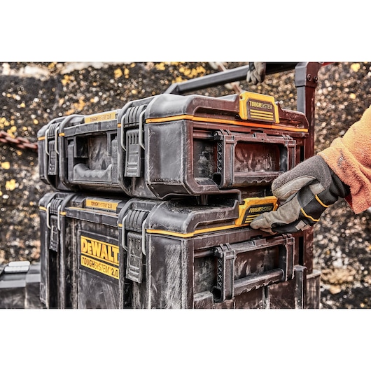 Stacked DEWALT ToughSystem 2.0 toolboxes are secured by a gloved hand outdoors.