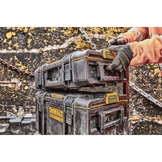 DWST83293-1 DEWALT ToughSystem toolboxes stacked, gloved hand adjusting top case outdoors.