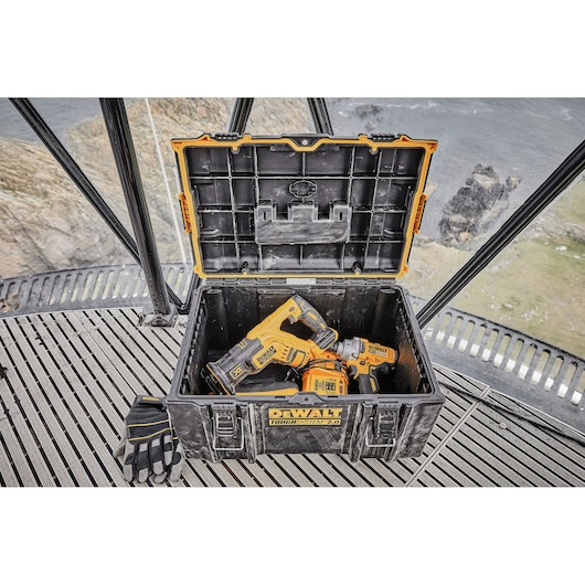 Open DEWALT Toughsystem 2.0 toolbox with power tools and gloves on a metal grate near a rocky coast.