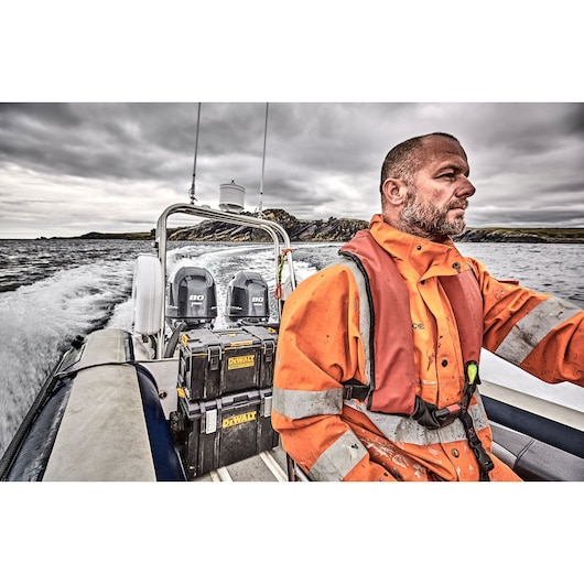 DEWALT toolboxes on a boat with a person in orange safety gear navigating through water under cloudy skies.