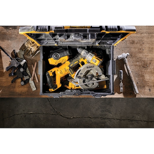 DEWALT ToughSystem toolbox open, containing power tools on a workbench with various hand tools around.