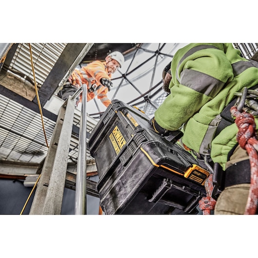 DEWALT tool box being carried by a worker in safety gear on an industrial site with another worker above.