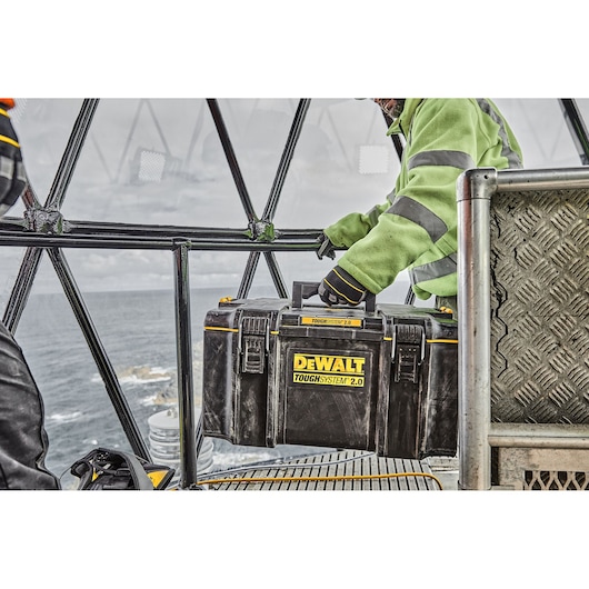 A worker carries a DEWALT ToughSystem 2.0 toolbox inside a metal structure near the sea.