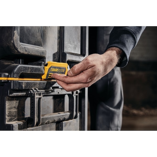 Hand operating the yellow latch on a DEWALT TOUGHSYSTEM storage box in a workshop setting.