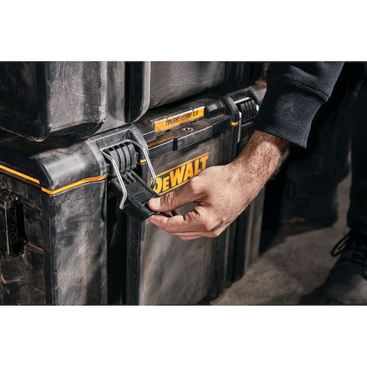 Hand unlatching a DEWALT ToughSystem 2.0 tool storage box with rugged, black and yellow construction.