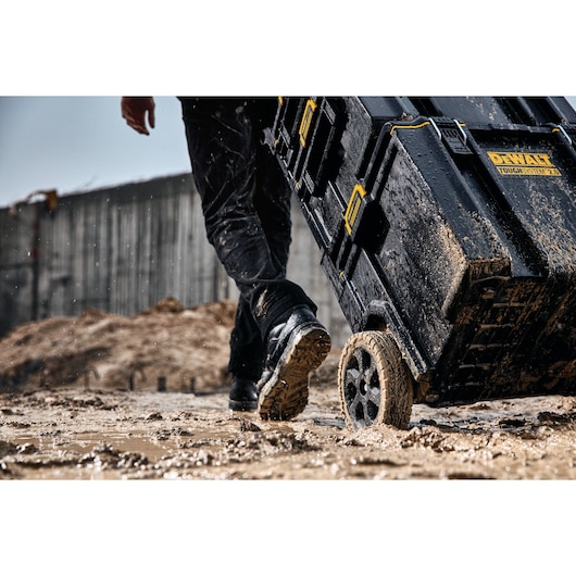 Muddy DEWALT ToughSystem 2.0 toolbox on wheels being pulled across a wet, muddy construction site.