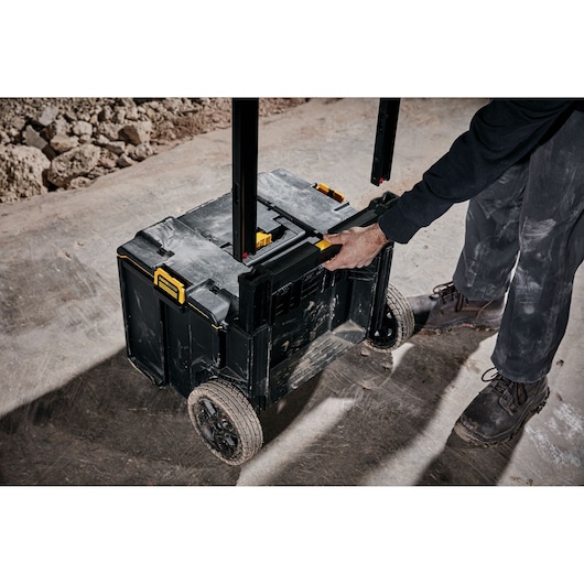 Person pulling a DEWALT rolling tool box with handle on a construction site floor.