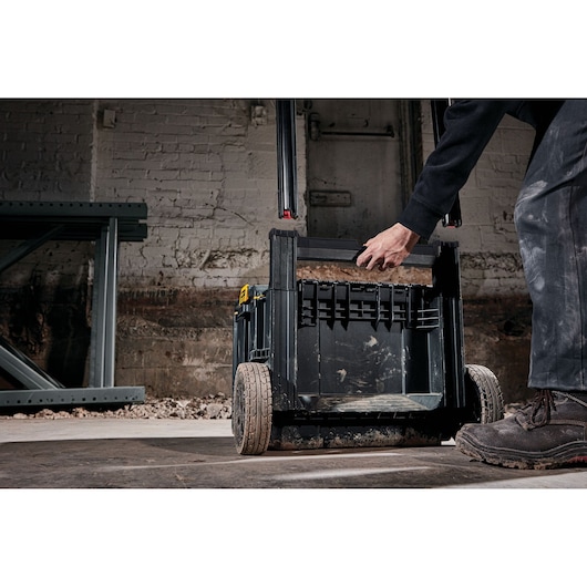 Person holding handle of DEWALT mobile tool box with wheels in a workshop setting.