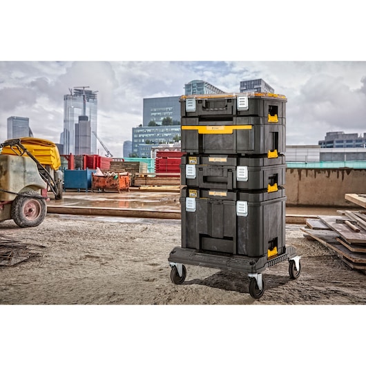 Stacked DEWALT toolboxes on a wheeled base at a construction site with buildings in the background.