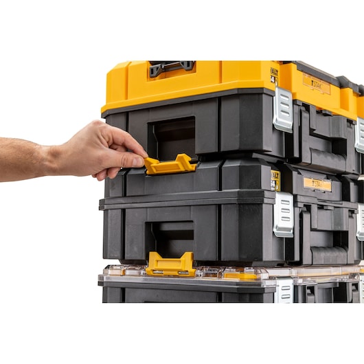 Hand unlocking stacked DEWALT black and yellow toolboxes using front yellow latch.