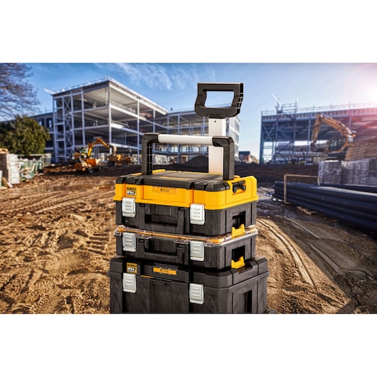Stacked DEWALT toolboxes with handle on a construction site, metal frames and machinery visible in background.