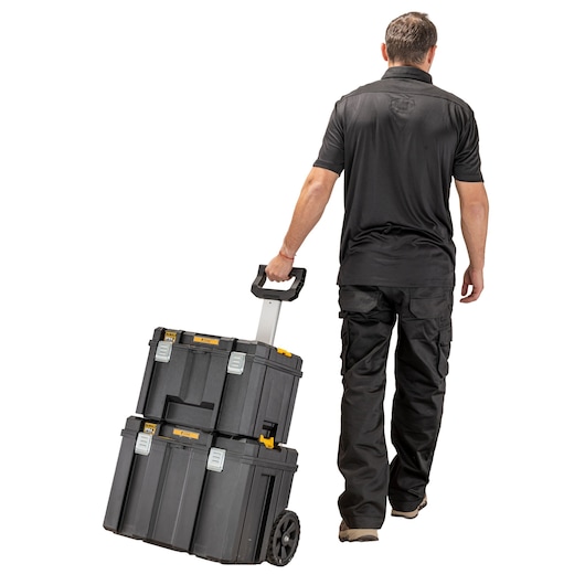 Person pulling stacked DEWALT storage boxes with wheels and handle. Boxes are black with yellow accents.