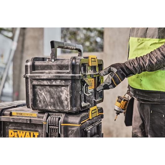 Gloved hand opens DEWALT Toughsystem 2.0 tool box stacked on another box at a worksite.