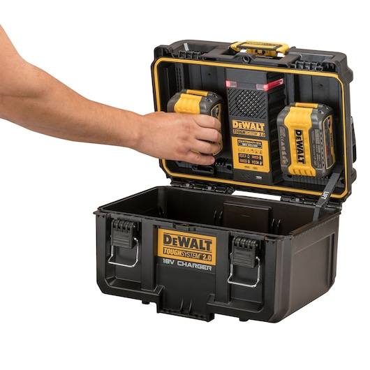Hand placing battery in DEWALT ToughSystem 2.0 18V charger case. Two batteries shown in lid compartment.